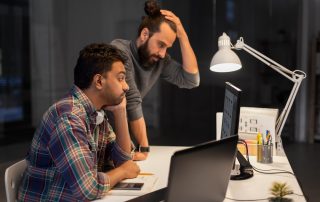 Technology problems concept. Men with hand on head working at desk in dark office.